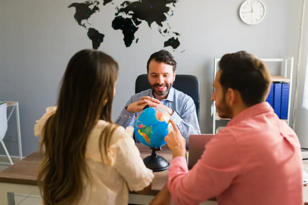 Consultor de turismo explicando destinos a um casal usando um globo terrestre em um escritório moderno, com mapa-múndi ao fundo.