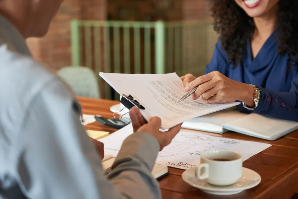 Duas pessoas analisando documentos com gráficos e contratos em ambiente corporativo, representando negociação ou revisão de acordo.