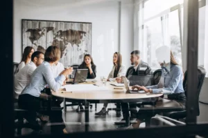 Grupo de profissionais em reunião de trabalho, discutindo estratégias de negócios em uma sala moderna com laptops e uma mesa redonda.