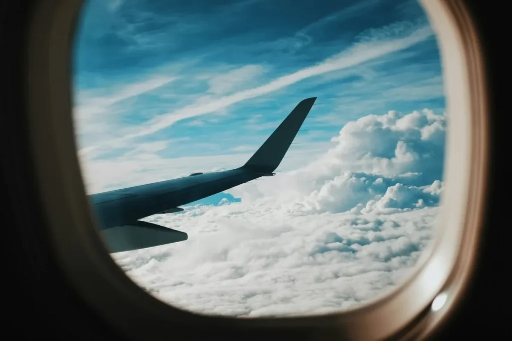 Asa de avião vista pela janela com céu azul e nuvens durante voo