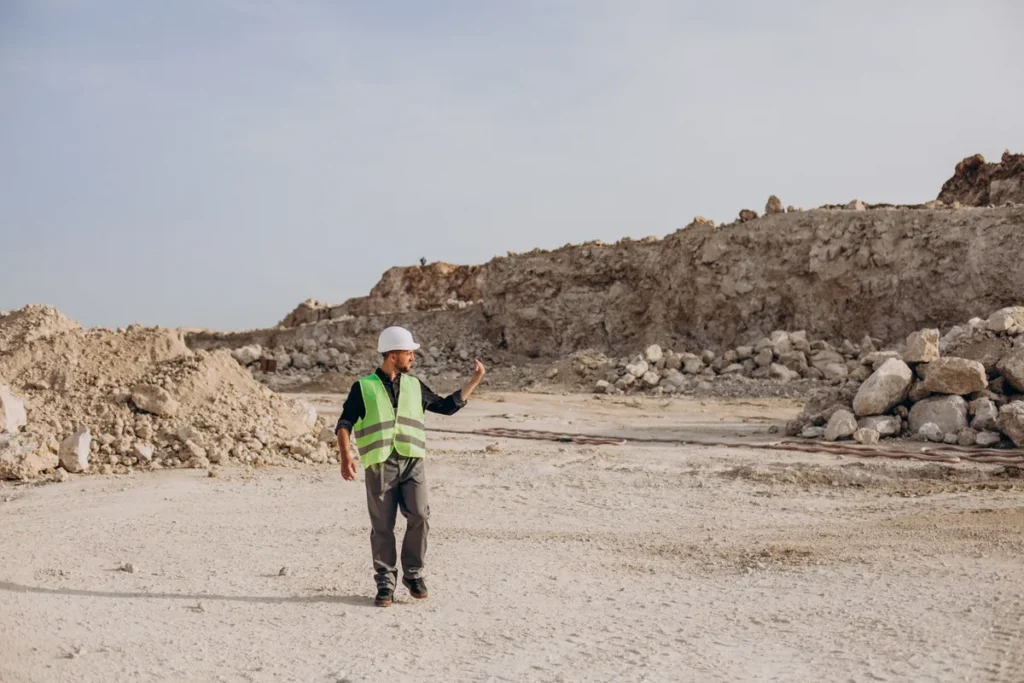 Geólogo de capacete e colete de segurança em pedreira ou mina, analisando o terreno e a geologia do local.