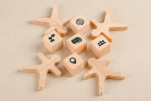 Peças de madeira em forma de pessoas cercando blocos com ícones de comunicação, localização, rede e trabalho em equipe sobre fundo bege.