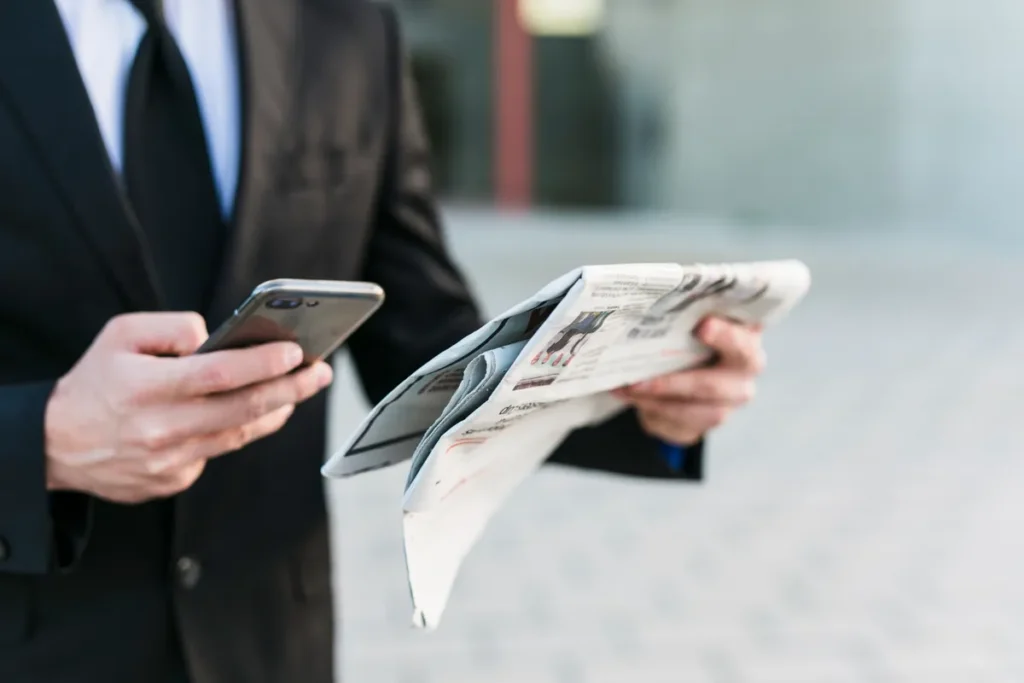 Homem de terno segurando jornal e smartphone, ilustrando a disseminação de notícias e a importância de um press release eficaz.