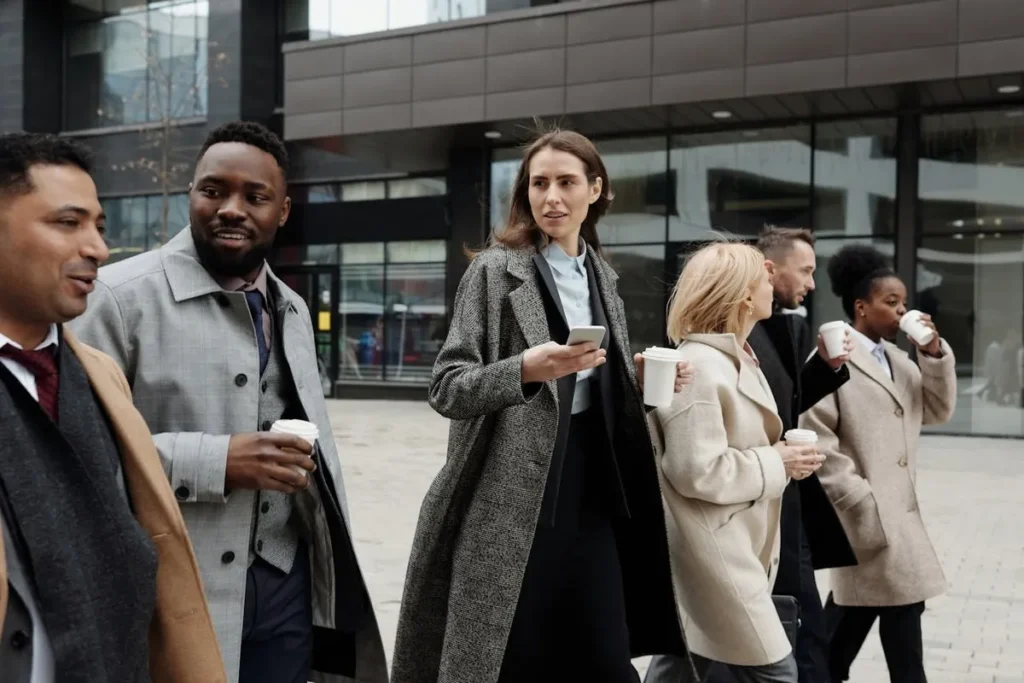 Grupo de profissionais diversos caminhando em área urbana com cafés, representando a colaboração e diferentes tipos de liderança em equipe.