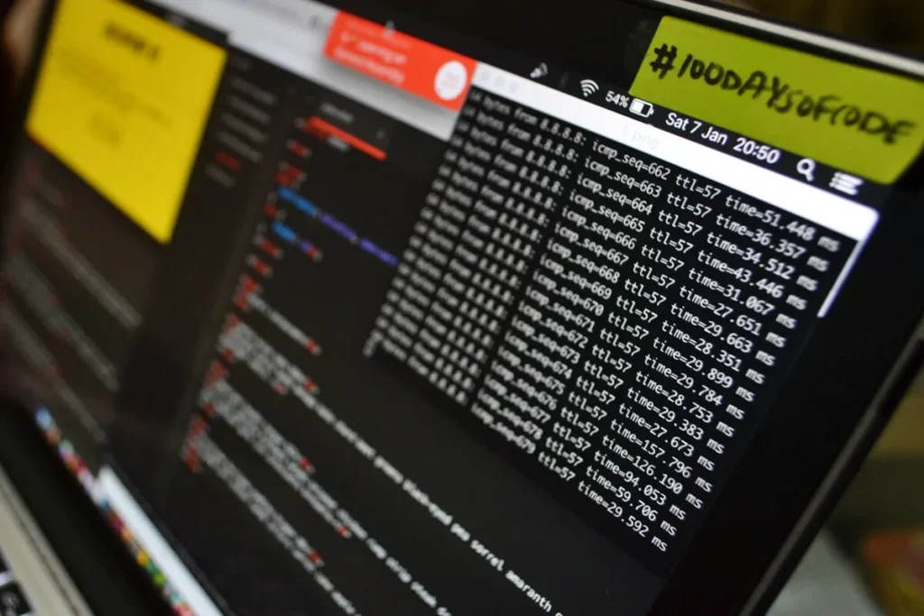 Uma tela de computador exibindo código e dados de rede, com a hashtag #100daysofcode em um post-it, representando o trabalho em cybersecurity.