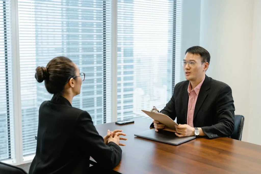 Dois executivos, um homem e uma mulher, conversando em uma mesa de conferência. A imagem destaca a importância da comunicação e da preparação para entrevistas em inglês.

