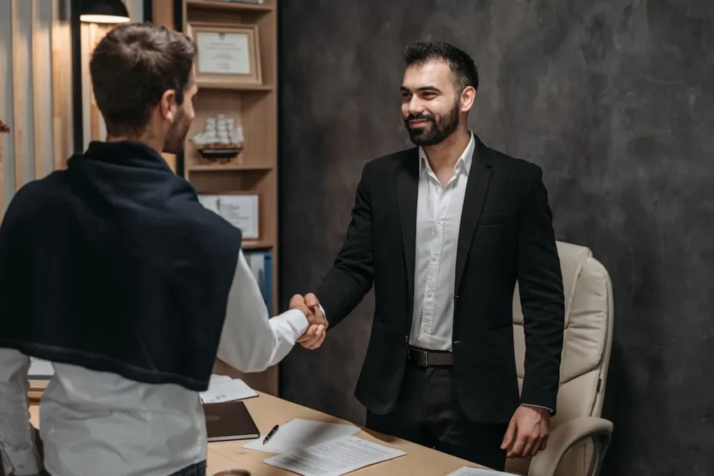 Dois homens de negócios apertando as mãos em um escritório, representando acordos de exportações.
