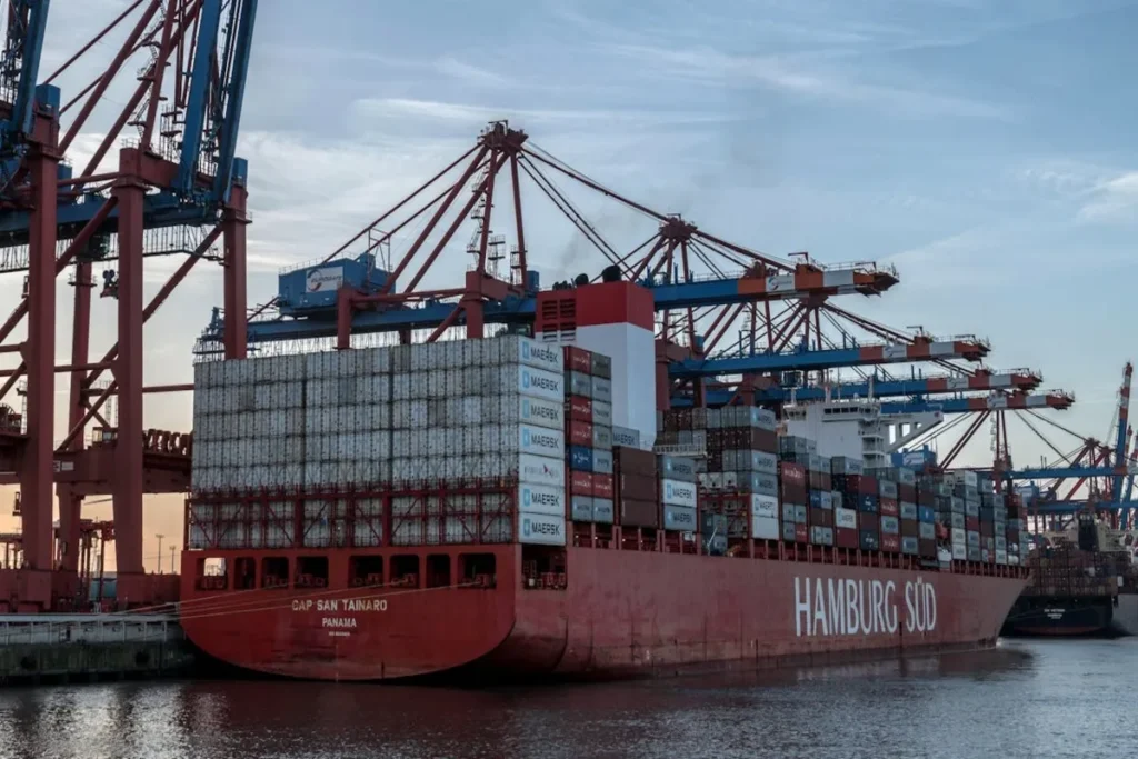 Navio de carga "Hamburg Süd" com contêineres e guindastes em um porto.