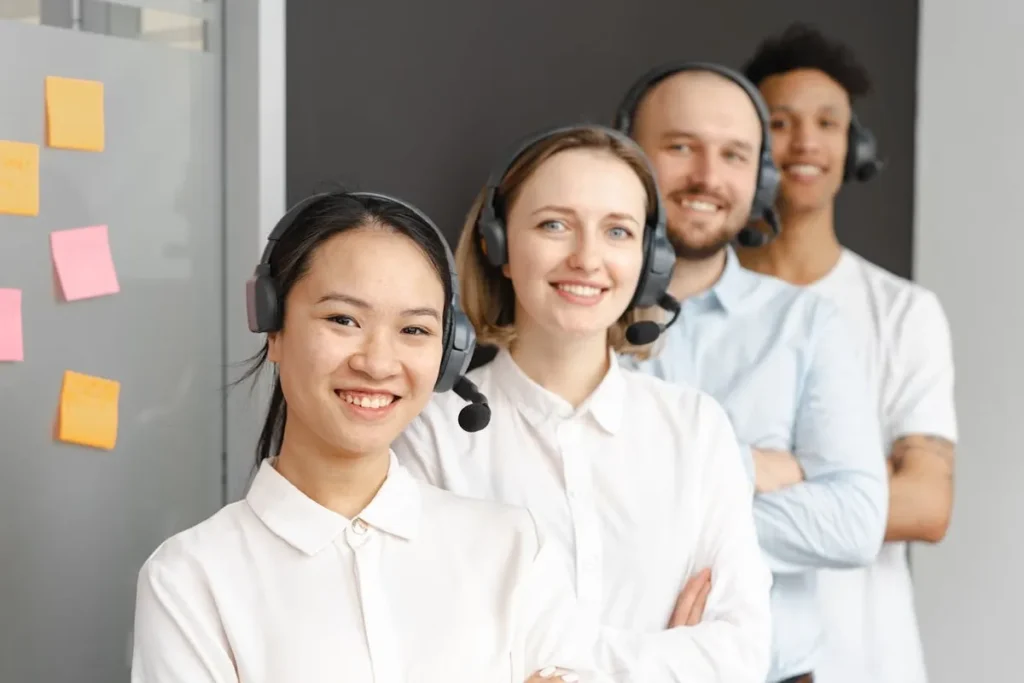 Pessoas sorrindo, usando fones de ouvido e headsets. A imagem destaca a importância do inglês básico para o atendimento ao cliente e a comunicação.