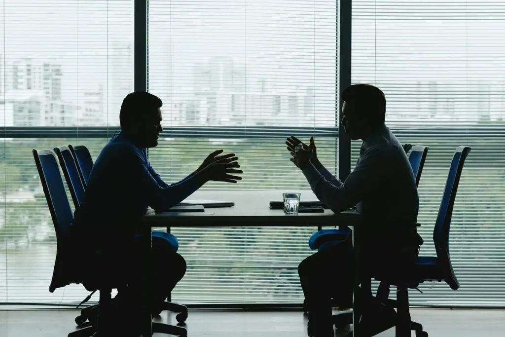 Dois executivos sentados frente a frente em uma sala de reuniões, discutindo estratégias de negócios em ambiente corporativo moderno