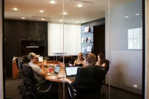 Quatro profissionais em uma reunião de onboarding em uma sala de conferências moderna, sentados ao redor de uma mesa oval com laptops abertos e discutindo estratégias.