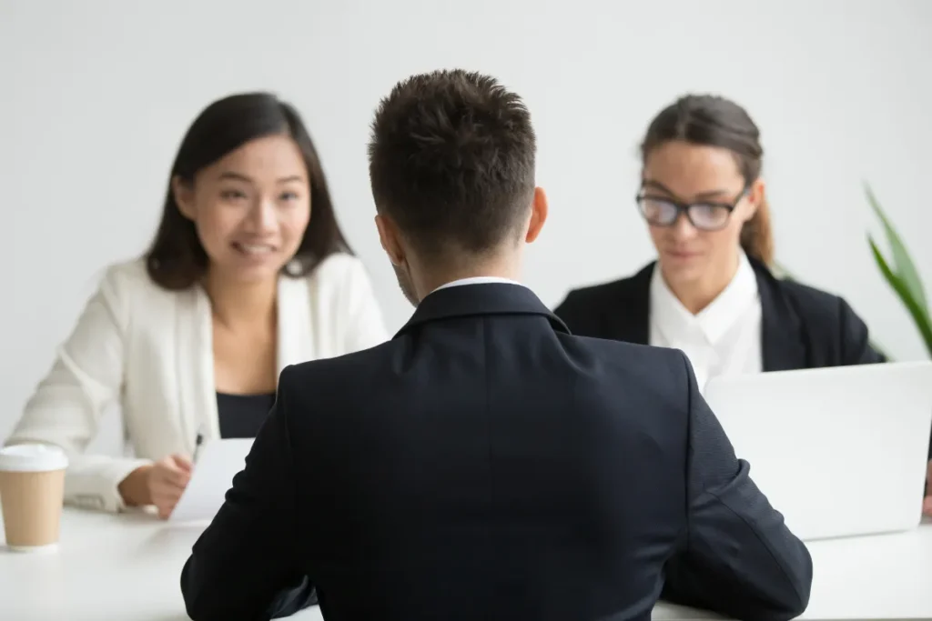 Profissional sentado de costas conversando com duas pessoas durante uma reunião em um escritório.