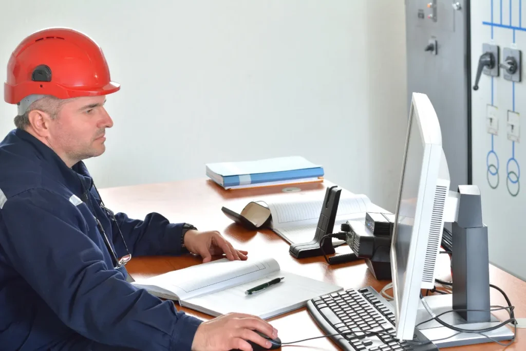 Engenheiro usando capacete de segurança enquanto trabalha em um computador em uma mesa de escritório.