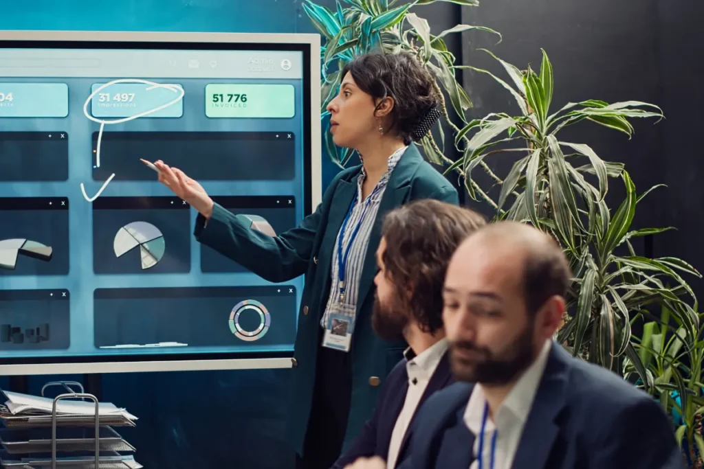 Executivos observando um painel digital com gráficos e dados enquanto discutem informações em um escritório.