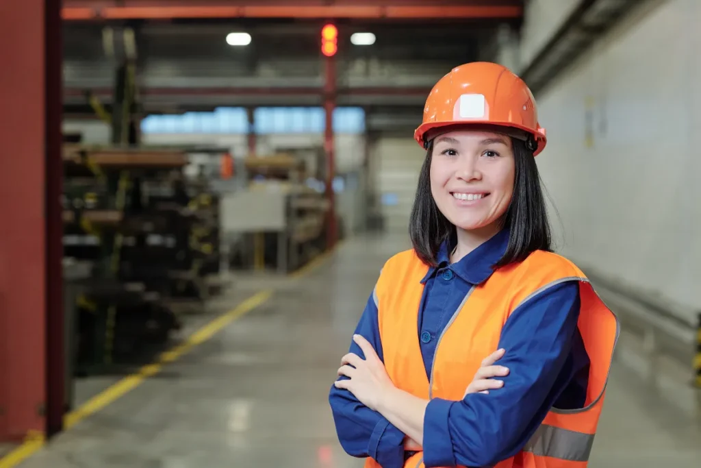 Profissional com capacete e colete de segurança em pé dentro de uma fábrica industrial.