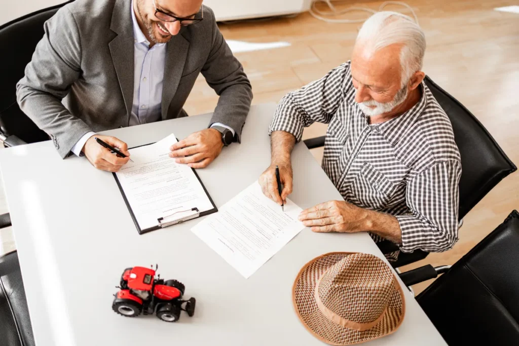 Dois produtores analisando documentos e fazendo anotações em uma mesa com um pequeno trator de brinquedo.