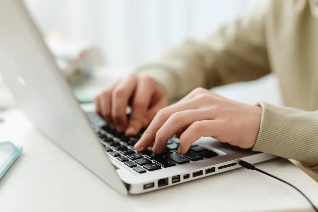 Mãos digitando em um notebook enquanto a pessoa trabalha em um computador portátil.