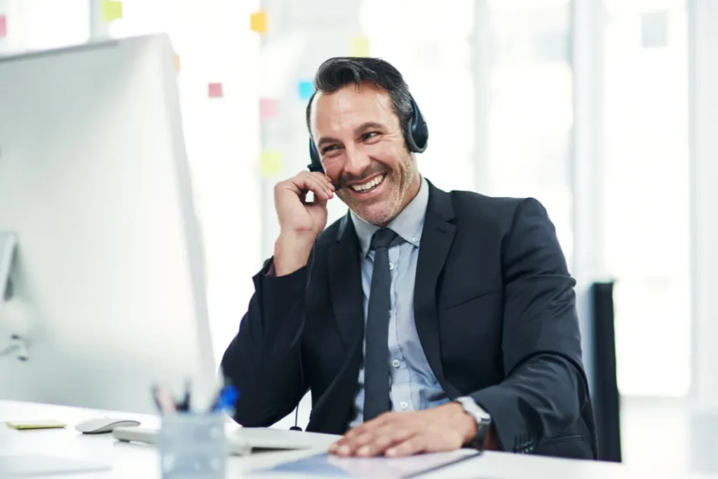 Profissional de atendimento ao cliente usando headset enquanto conversa com um cliente em frente ao computador no escritório.