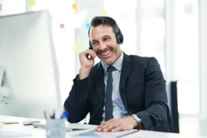 Profissional de atendimento ao cliente usando headset enquanto conversa com um cliente em frente ao computador no escritório.