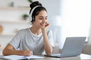mulher usando fones de ouvido estudando no notebook e fazendo anotações em um caderno
